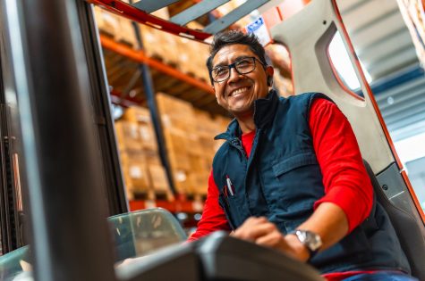 Happy latin worker smiling at camera while using forklift in a distribution warehouse